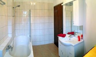 A modern bathroom with a bathtub, a shower, and a sink. The walls are tiled and there is a wooden door in the background.