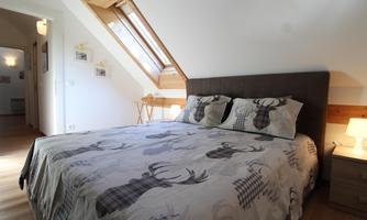 A cozy bedroom with a large bed and an animal motif on the bedspread. The room has a sloped window and a warm atmosphere.
