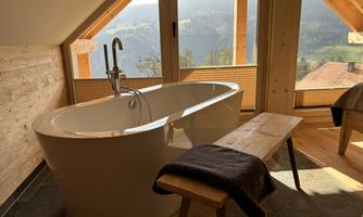 A modern bathroom with a freestanding bathtub and a view of the mountains. Large windows let in plenty of light and create a relaxed atmosphere.