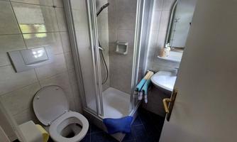 A small bathroom with a shower, sink, and toilet. Towels and bathroom accessories are visible.