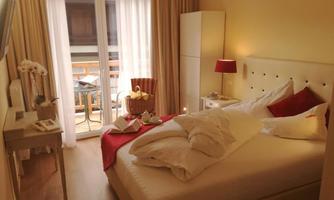 A bright and cozy bedroom with a large bed and red accents. Natural light streams in through the windows, providing a view of a balcony.