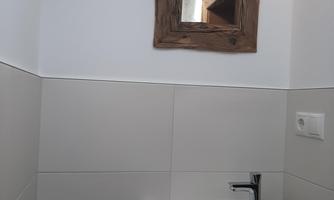 A modern bathroom with a sink and a small wooden mirror. A blue towel hangs on the wall.