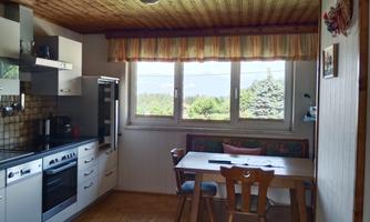 A bright kitchen with modern appliances and a table with chairs. Large windows offer a view of the outdoors.