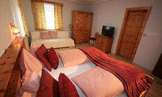 A cozy bedroom with two beds and a daybed. Wooden cabinets and a television enhance the inviting atmosphere.