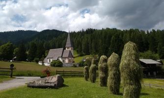 A picturesque landscape with a church and large green hills. In the foreground, there are futuristic hay bales and a tree trunk.