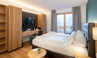 A modern hotel room with wooden shelves and a double bed. Large windows let in plenty of daylight and provide a view outside.