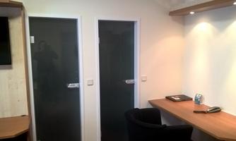 A modern room with two glass doors and a desk. There are some items on the desk, and the wall is brightly lit.