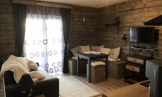 A cozy living room with a modern sofa, a dining table, and a TV corner. Large windows let in plenty of light, and the wood look creates a warm atmosphere.