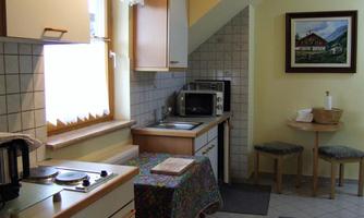 A small, cozy kitchen with a dining table and two chairs. The walls are painted light and the windows let in a lot of light.