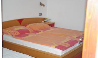 A cozy bedroom with a large double bed and colorful bedspreads. Next to the bed is a small bedside table with books.