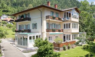 A charming three-story house with balconies and colorful flowers. Surrounded by green meadows and trees in a picturesque landscape.