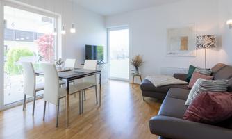 Bright living room with a modern sofa and a dining table. Large windows bring lots of daylight into the room.