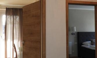 A hallway with an open door to a room. On the left side, there is a table with chairs and a window with curtains.