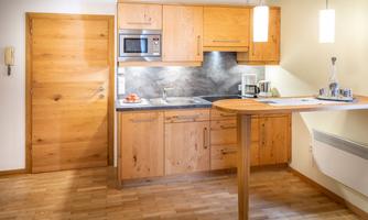 A modern kitchen with wooden cabinets and a handleless countertop. The equipment includes a stove, a microwave, and a coffee machine.