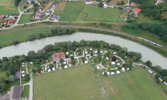 An aerial view of an area with a football field, residential areas, and a river. The image shows campsites and surrounding trees.