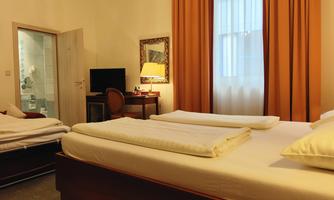 A cozy room with two beds, a desk, and a TV. The large windows let in plenty of daylight.
