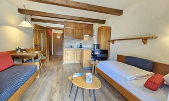 A cozy room with wooden beams and a small kitchenette. There is a seating area with a table and two sofa beds.