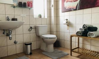 A modern bathroom with beige tiles and a sink. Fresh towels are lying on a shelf, and a large piece of artwork hangs on the wall.