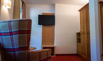 A cozy room with an armchair and a modern television on the wall. The floor is covered with a red carpet, and there is a wooden table.