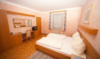 A simple room with two single beds and wooden furniture. There is a desk, a television, and carpet flooring.