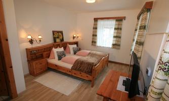 A cozy bedroom with a double bed and wooden work furniture. It is well-lit and has a window with curtains.