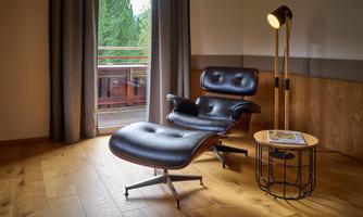 A stylish room with a comfortable black armchair and a matching footstool. Next to the armchair is a modern floor lamp and a small table.
