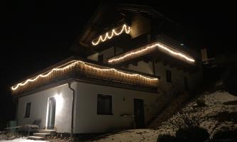 A pretty house in the snow, illuminated with festive lights. The surroundings are dark, which makes the lights stand out beautifully.