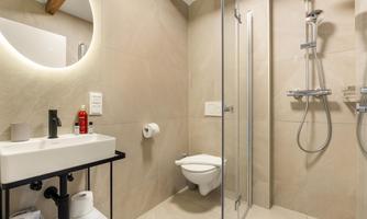 A modern bathroom with a glass shower cabin and an elegant sink. The walls are in neutral colors, and there is a round mirror light.
