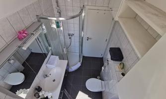A modern bathroom with a shower, sink, and mirror. The walls are tiled, and there is a bright atmosphere.