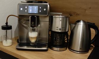 A modern coffee machine stands on a wooden surface. Next to it are a drip coffee maker and a kettle.
