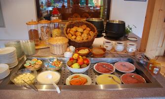 A selection of breakfast options on a table. There are rolls, sausage, cheese, fruit, and various cereals.