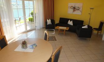 A bright living space with a round table and black sofa. Large windows offer a view of nature outside.