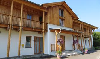 A modern building with a wooden facade and large windows. The entrance area is designed in a friendly way and adorned with flowers.