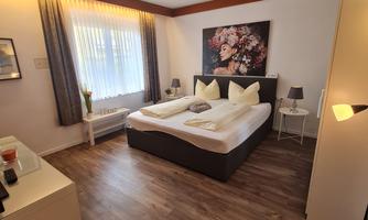 A modern bedroom with a large bed and hardwood floor. The room is bright and cozy, with a beautiful piece of artwork on the wall.