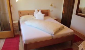 A cozy bedroom with a large bed and decorative pillows. The room is bright and friendly designed, with a wooden wardrobe and a mirror.