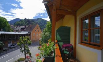 A cozy balcony overlooking a quiet street and adjacent houses. In the background, mountains and a clear sky can be seen.