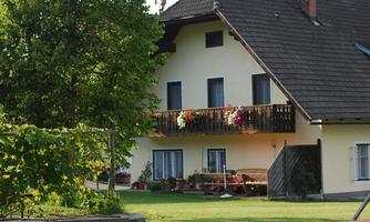 A cozy house with a balcony and flower boxes. The garden is green with a table and a fire pit.