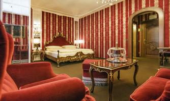 An elegant hotel room with red striped walls and a large double bed. Comfortable red armchairs and a stylish table complement the furnishings.