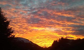 A breathtaking sunset with glowing orange and red clouds. The silhouettes of trees and mountains complement the picturesque scene.