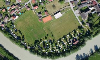 Aerial view of a residential area with many houses and green spaces. Nearby, a river flows, surrounded by trees and meadows.