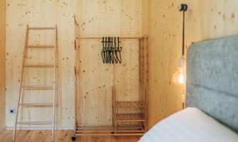 A bright room with wood paneling and a cozy bed. A wooden ladder and a clothes rack stand against the wall.