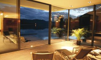 A modern living room with large glass windows and a view of a tranquil lake. The lighting creates a cozy atmosphere in the evening.