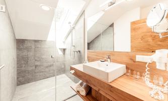 A modern bathroom with clean lines and bright tiles. The wooden sink unit and the glass shower cubicle give the room an elegant atmosphere.