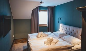 A modern bedroom with a comfortable double bed and soft colors. The tranquil atmosphere is emphasized by the windows with curtains and the subtle lighting.
