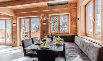 A stylish dining room with wooden paneling and large windows. The table is elegantly set and accommodates several guests.
