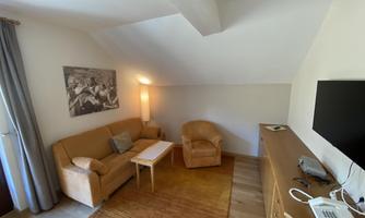 A cozy living space with a sofa and an armchair. A table and a television are also available.