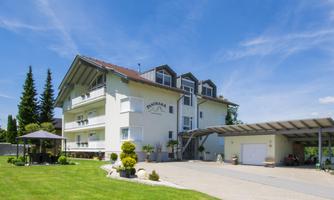 A modern building with several floors and a beautiful garden. Nearby is a carport and a covered area for relaxation.