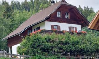 A traditional two-story house with a wooden roof. In front of the house is a well-maintained garden with bushes and plants.