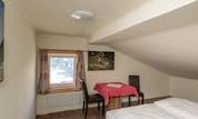A cozy room with a double bed and a table. The window offers a view outside and the walls are decorated with pictures.