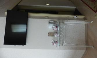Wall-mounted flat-screen TV above a white metal table with teapots, cups and an electric kettle; bathroom entrance on the right.